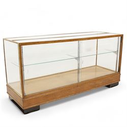 Early 20th century glazed oak and brass bound shop's display cabinet or haberdashery cabinet, fitted with two sliding glass doors, two glass shelves on chromed metal supports, black finish block feet