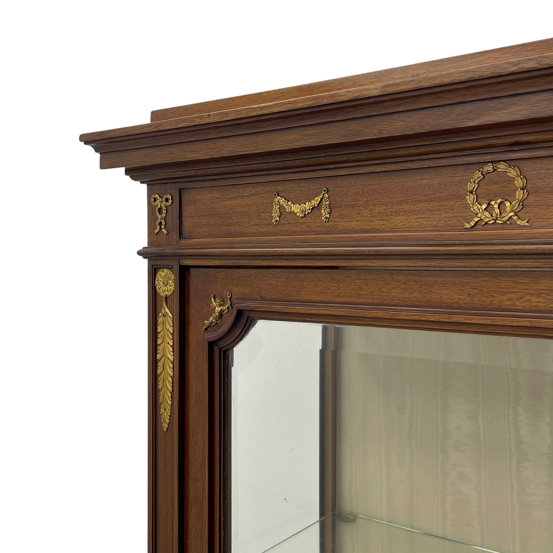 Early 20th century Louis XVI design mahogany vitrine display cabinet, projecting stepped cornice over recessed frieze decorated with gilt metal mounts of festoons and a bellflower wreath, fabric lined interior with two glass shelves, enclosed by bevel glazed door with lower panel, on two turned front feet 