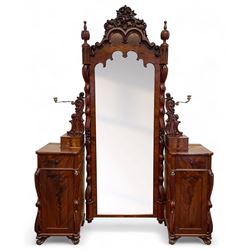 Tall Victorian figured mahogany twin pedestal dressing table, the tall mirror with flower head and scrolled leaf carved pediment, flanked by two turned and carved finials over faceted lancet arched lantern tops, plane mirror plate enclosed by shaped frame, pierced and undulating moulded uprights, on C-scroll and curled leaf carved supports fitted with cast brass hinged candle sconces, each pedestal fitted with two small trinket drawers over larger drawer and panelled cupboard, canted corners with matched upright mounts, the cupboard doors enclosing slides, on scroll carved feet 