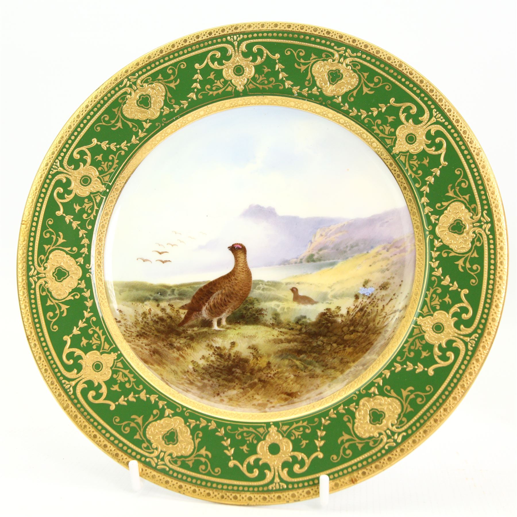 Early 20th century Royal Crown Derby porcelain twin handled vase, circa 1926, the central cartouche with a landscape, H16cm, Coalport cabinet plate centrally painted with a Red Grouse in a Highland landscape, within a green and gilt raised border, D22cm, together with a Coalport dish, hand painted with fruit against a pink and gilt ground (3)