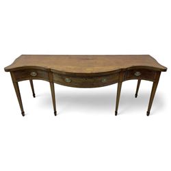 Large George III mahogany serpentine serving table, shaped top with crossing banding and stringing, the frieze fitted with three cock-beaded drawers, oval pressed brass handle plates decorated with urns, on square tapering supports with spade feet 