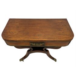 Regency inlaid rosewood card table, rectangular swivel and fold-over top with rounded corners and baize lined interior, the frieze decorated with a central ebony panel with applied gilt metal swan motifs, over a brass inlay band, raised on S-scroll supports united by concave platform base, terminating to out-splayed supports with brass cups and castors