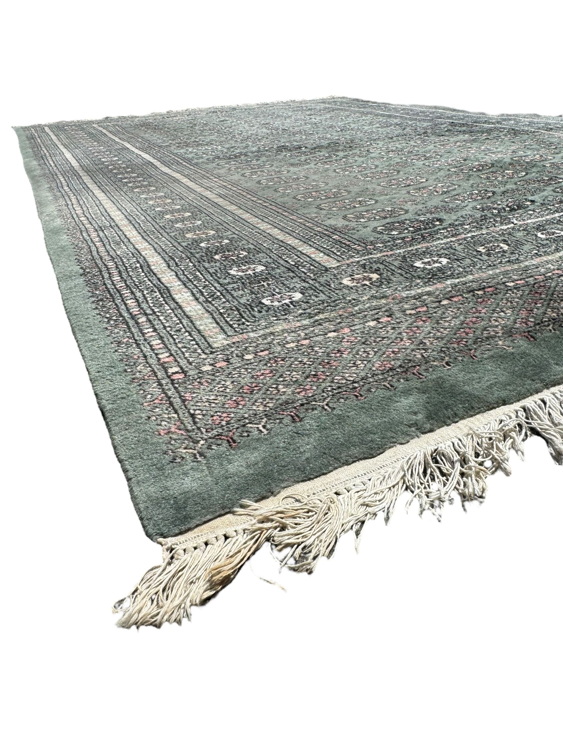 Pakistani Bokhara green ground rug, the field decorated with rows of repeating gul motifs, the main border featuring a series of smaller gul designs and geometric patterns, framed by multiple guard stripes