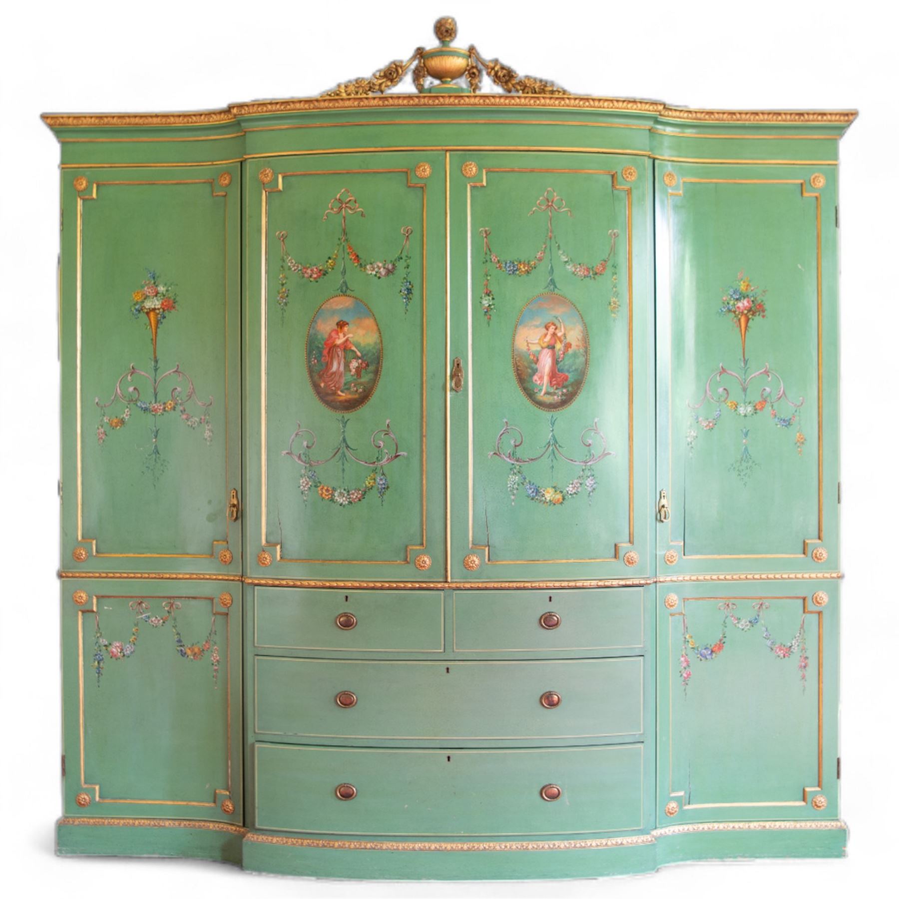 Edwardian Adam Revival break-bowfront quadruple green-painted and parcel gilt wardrobe, the projecting acanthus leaf moulded cornice surmounted by urn with trailing flower heads, two central panelled doors enclosing linen slides, decorated with oval painted panels depicting maidens with flowers and scrolled acanthus leaves with floral festoons, two short and two long drawers below, flanked by full-height panelled doors enclosing hanging rails and hooks, foliate moulded plinth base