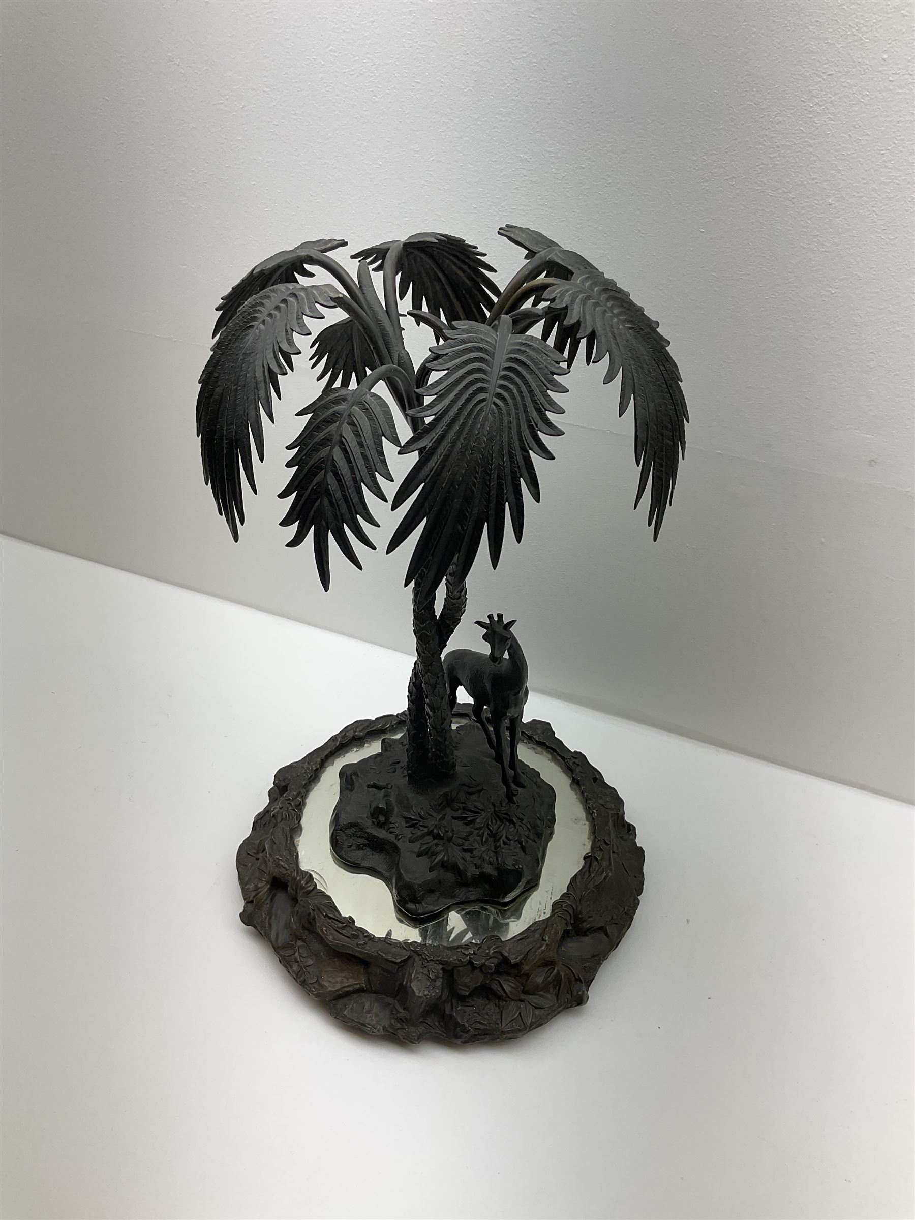 Sculpture of a giraffe under a palm tree upon a mirrored base, H48cm