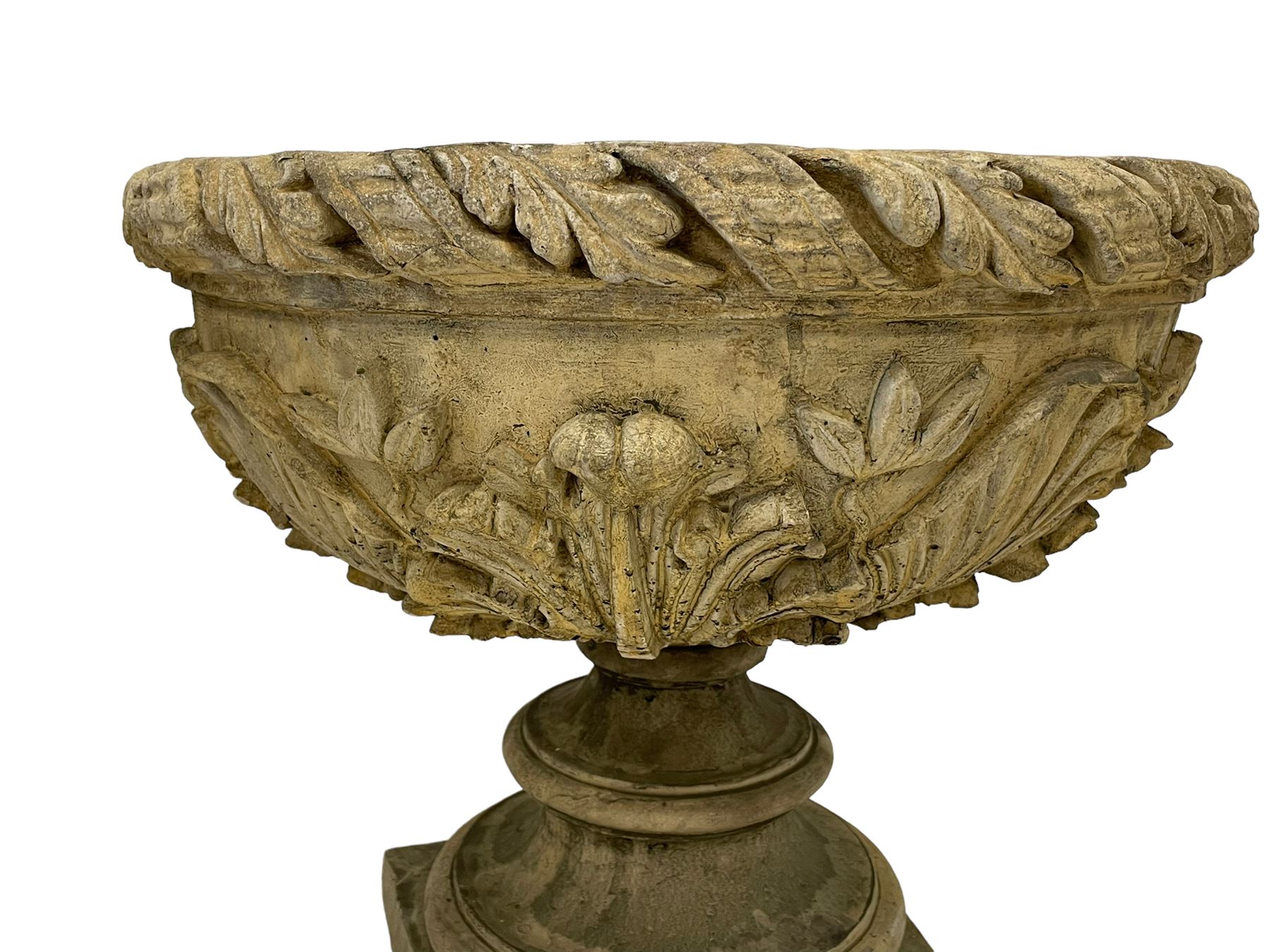 Pair of composite stone garden urn planters, acanthus leaf garland rim over foliate decorated body, stepped foot on square base