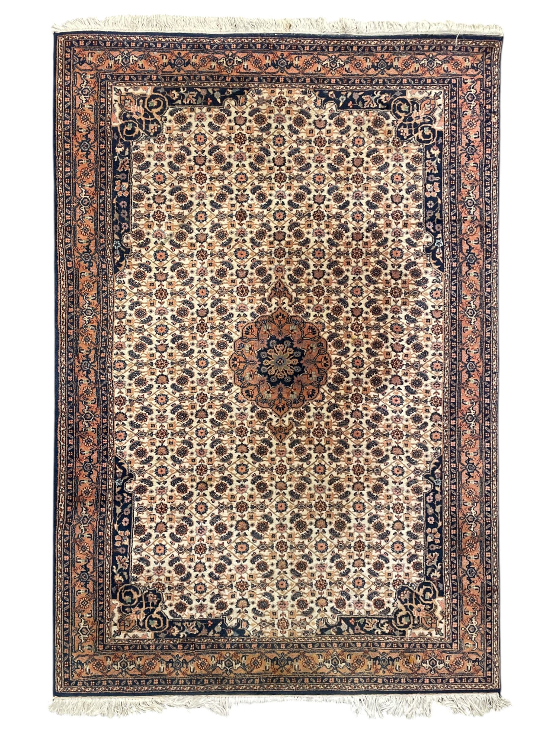 Indo-Persian Herati design ivory ground rug, central medallion on a field of repeating floral Herati motifs, peach ground border with repeating pattern, enclosed by guard stripes 