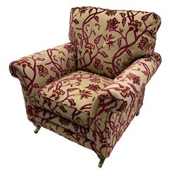 Contemporary upholstered armchair, scroll arms and loose cushions, embossed beige ground fabric with red and gold floral motifs, on tapered wooden supports with front brass castors