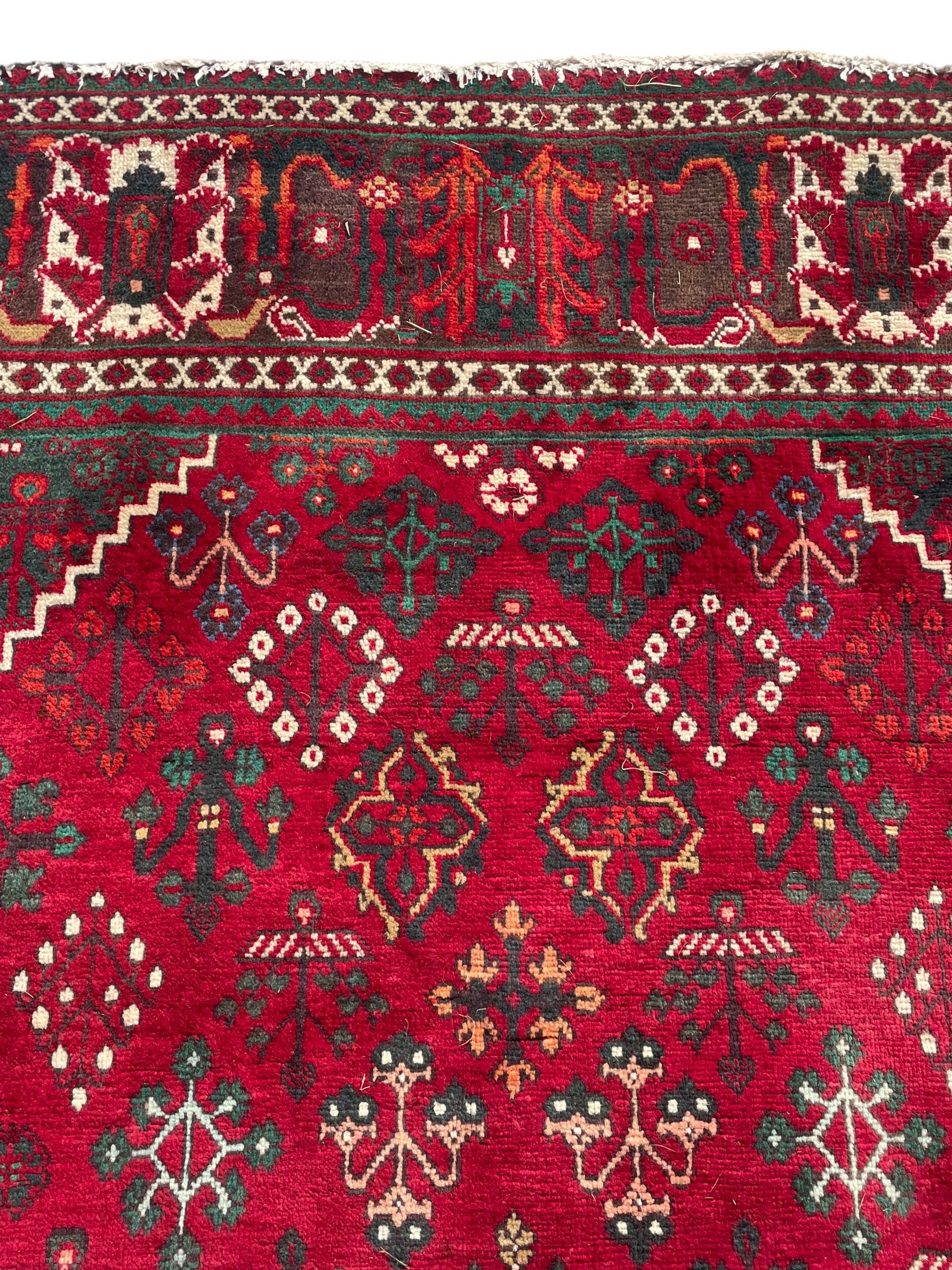 Persian Meymeh red ground rug, stepped lozenge medallion and spandrels, decorated all over with tree of life motifs, the main border decorated with repeating stylised plant motifs within geometric guard stripes 