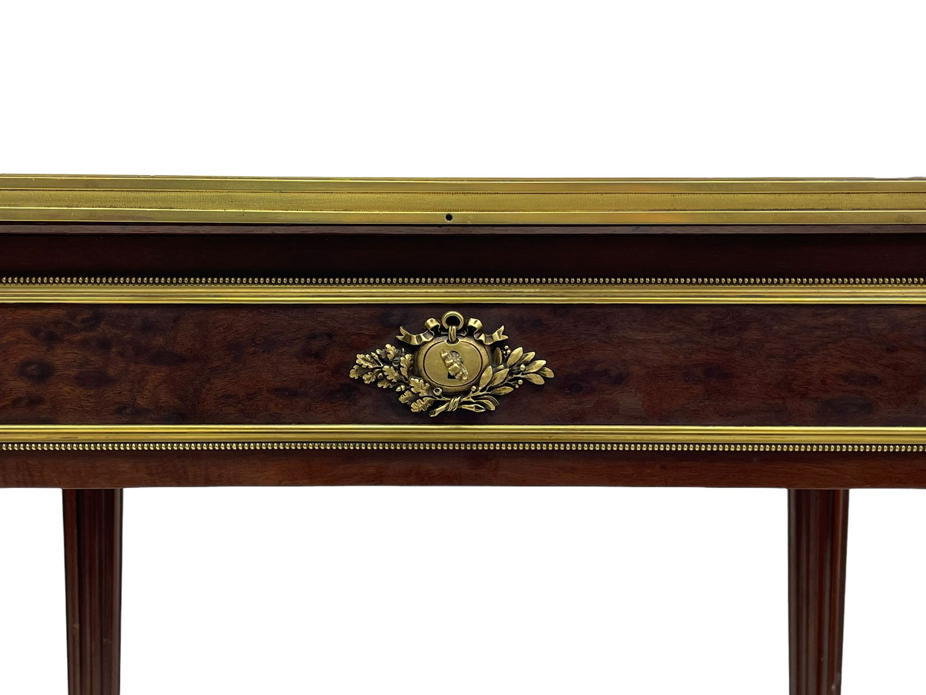 Late 19th century French figured plum pudding mahogany side table, canted rectangular white marble top with raised gilt metal gallery, fitted with a single frieze drawer, central extending floral cast ormolu escutcheon and applied moulded edging, on tapering turned and fluted supports with brass cups and castors, decorated with cast foliate mounts and foliate cast collars 