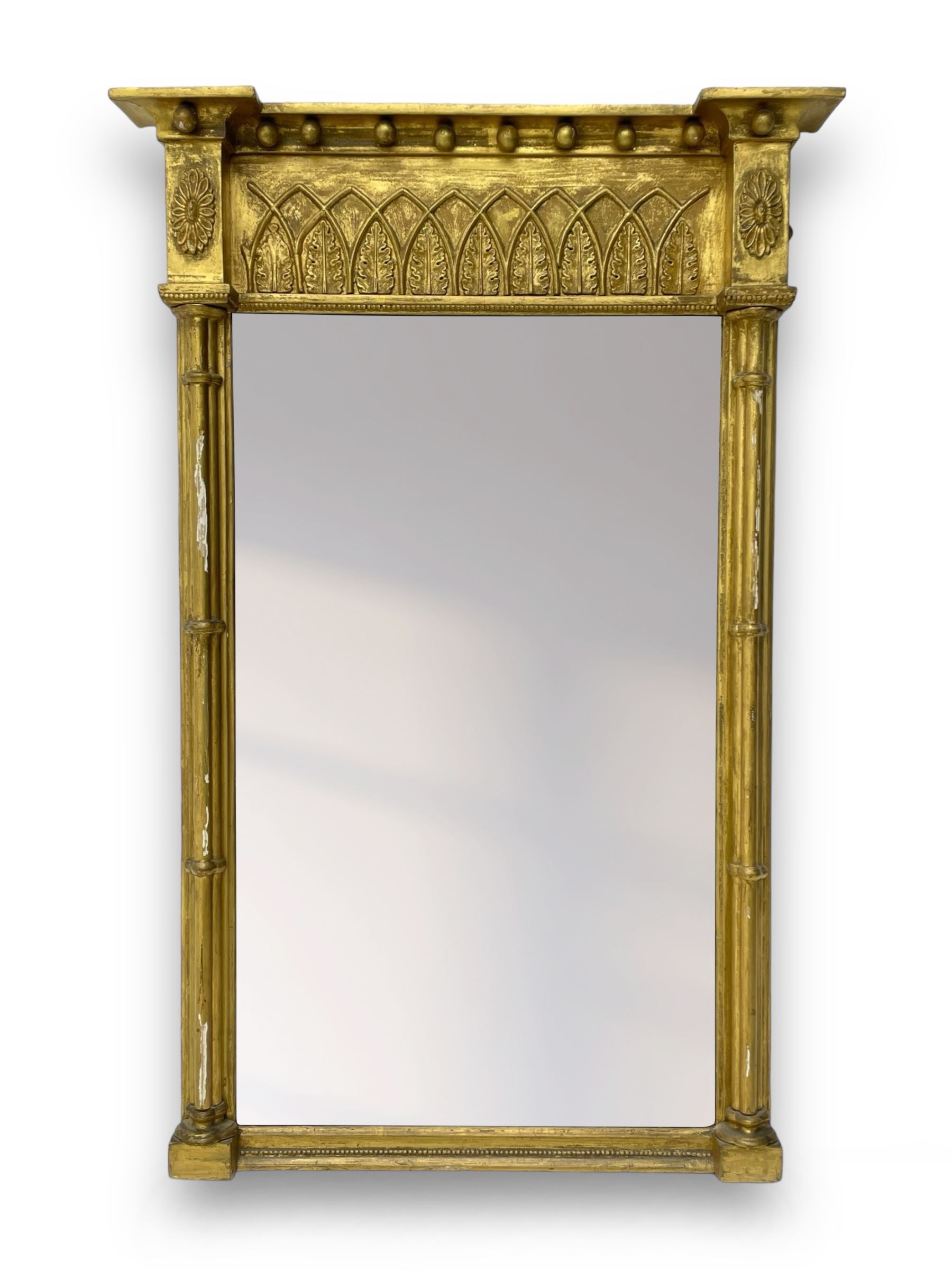 Regency giltwood and gesso pier mirror, projecting cavetto cornice with ball mounts, the frieze decorated with pointed arcade and foliate motifs, plain mirror plate enclosed by cluster column pilasters 