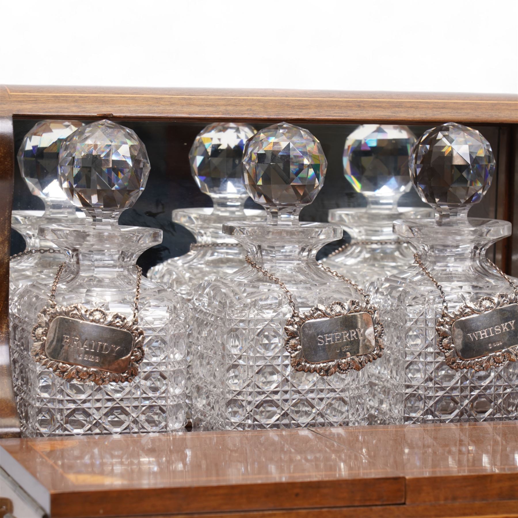 Edwardian walnut and boxwood inlaid tantalus games compendium, having three square section cut glass decanters, with associated silver Brandy, Sherry and Whisky labels, the two hinged doors with Bramah lock, open to reveal a fitted interior with four sherry glasses, over a secret sprung drawer to the base containing a selection of playing cards and cribbage board, L36cm x H32cm 