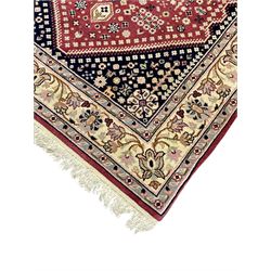 Persian design crimson ground rug, the field decorated with tree of life and floral motifs, enclosed by indigo spandrels with stylised flower head decoration, repeating scrolling border 