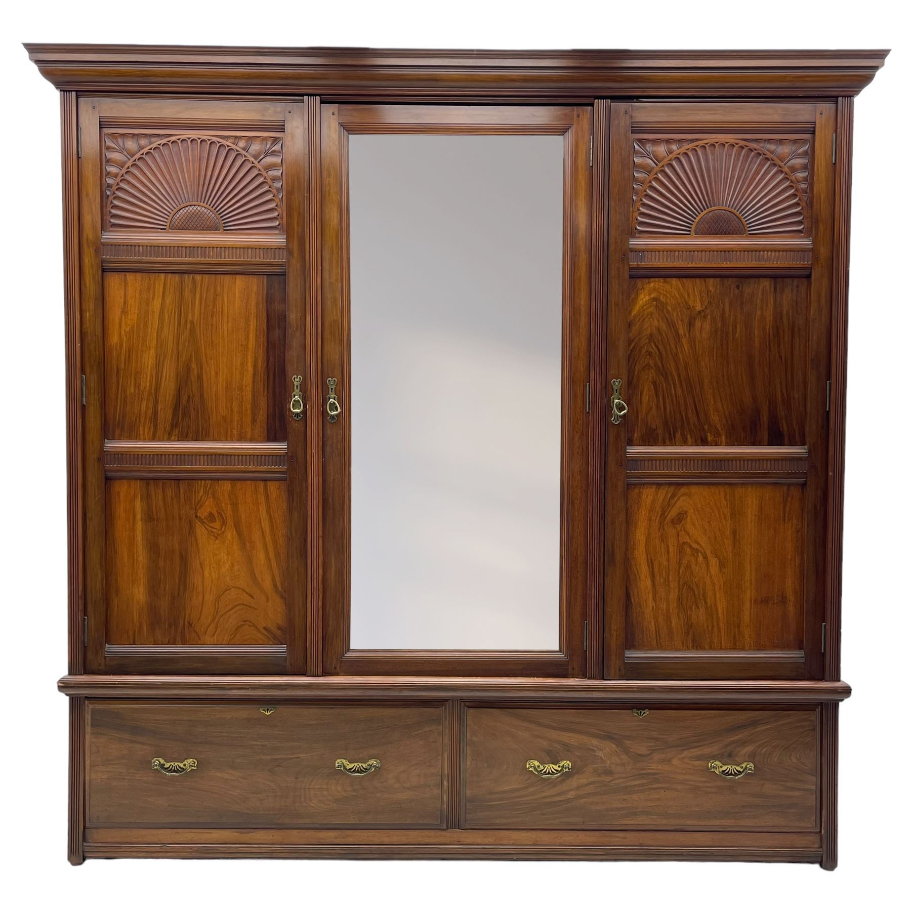 Late Victorian walnut triple wardrobe, projecting moulded cornice over central bevelled mirror door and flanking panelled doors, the top panels carved with fluted fans and stylised leaf motifs, the interior fitted with three linen slides, two drawers and hanging space, two long drawers to base, reed moulded uprights and vertical fluted horizontal rails 