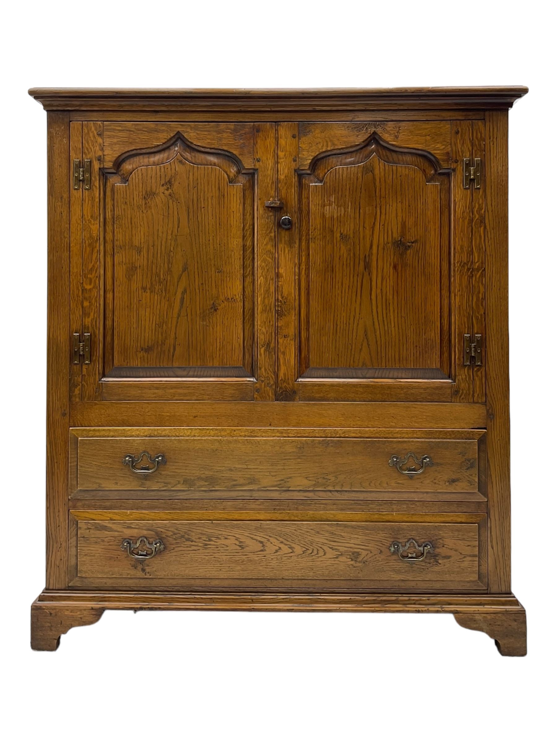 Oak drinks or media cabinet, projecting moulded cornice over two Gothic arch panelled doors on sliding tracks enclosing open storage, two drawers with brass drop handles, on bracket supports