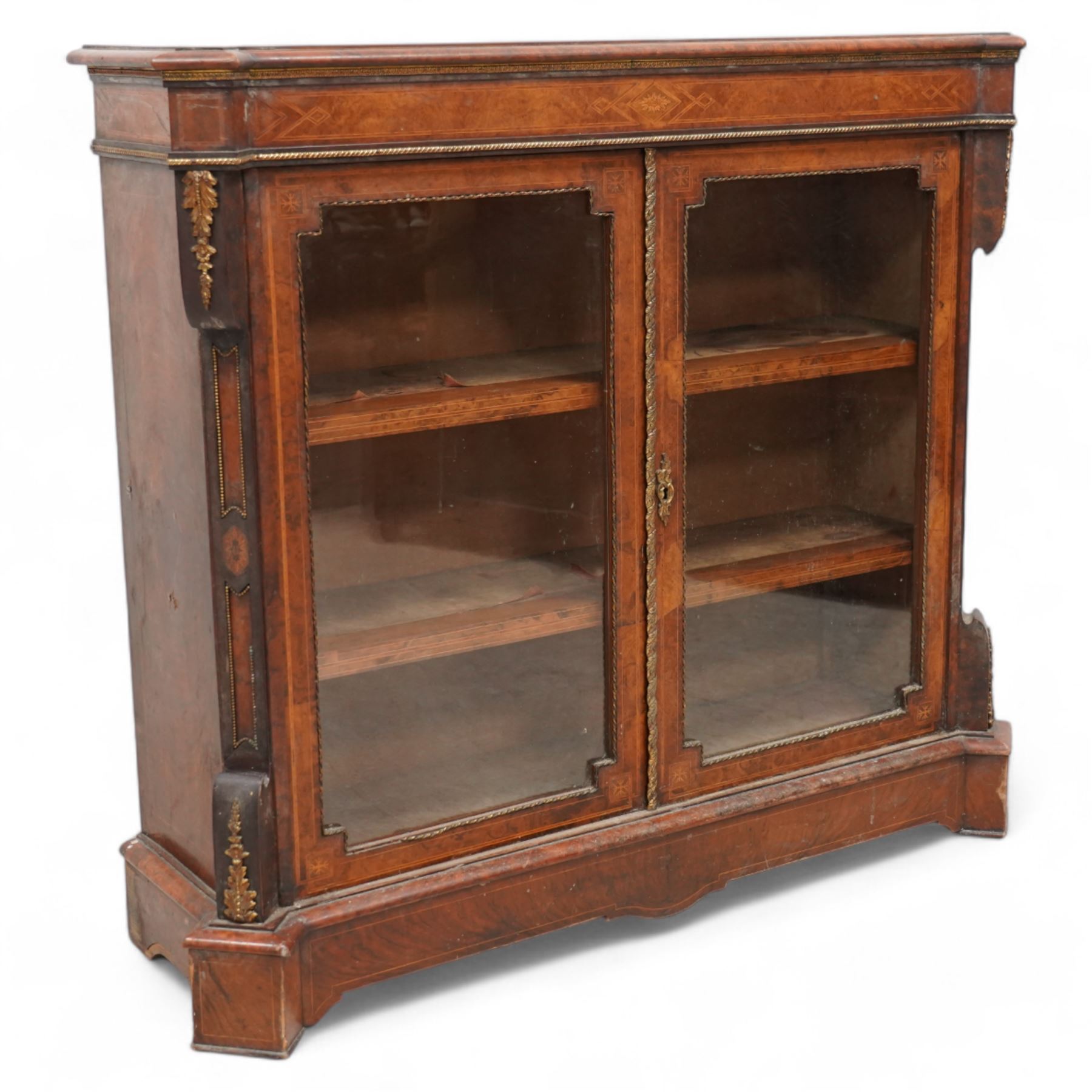 Victorian inlaid walnut and gilt metal mounted pier display cabinet, moulded rectangular top with extending square corners, the frieze inlaid with geometric satinwood bands and decorated with gilt metal edging, two glazed doors enclosing two shelves, enclosed by canted corners with recessed panels and gilt metal mounts, on moulded skirt base 