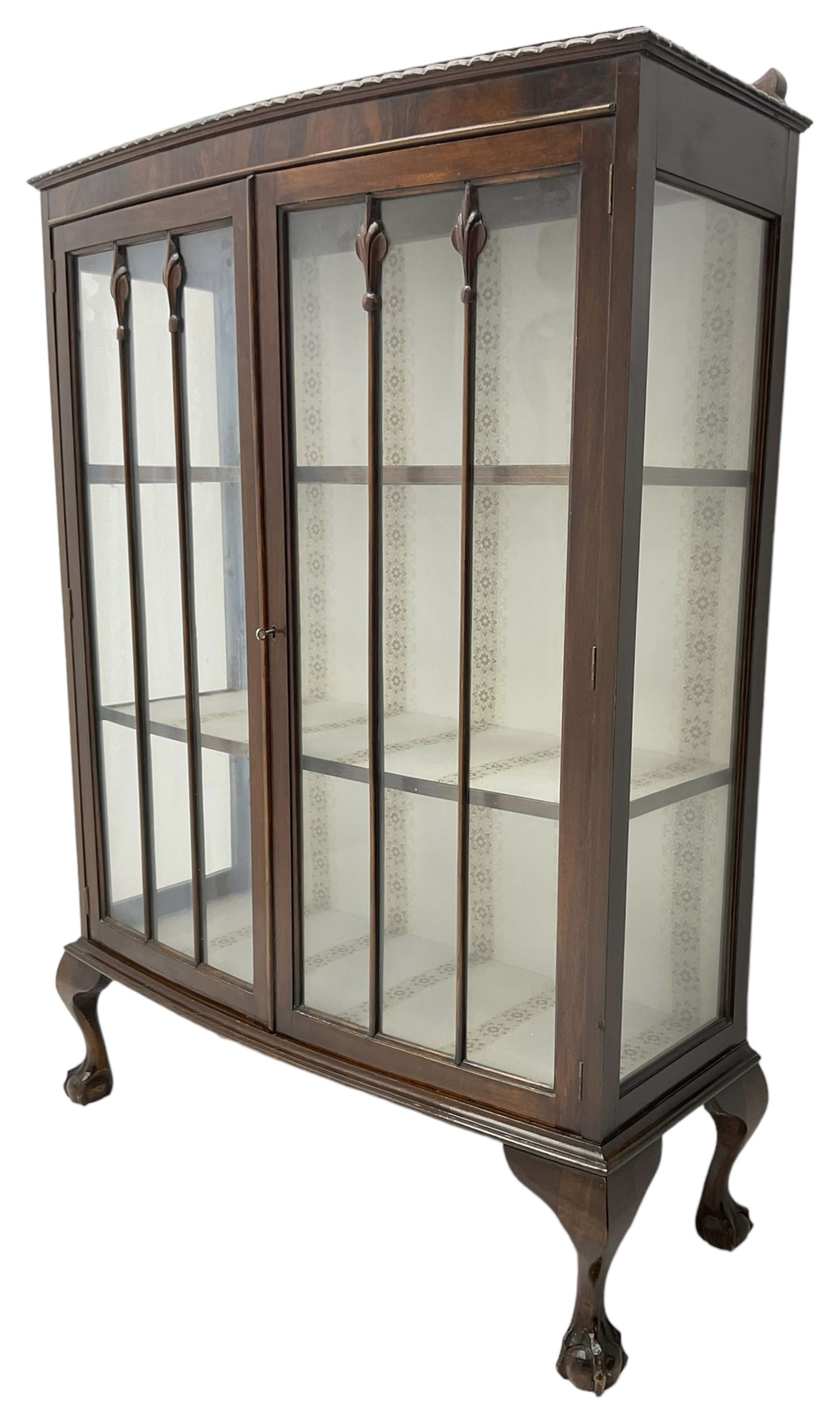 Early 20th century figured walnut bow-front display cabinet, enclosed by two glazed doors, on ball and claw cabriole feet