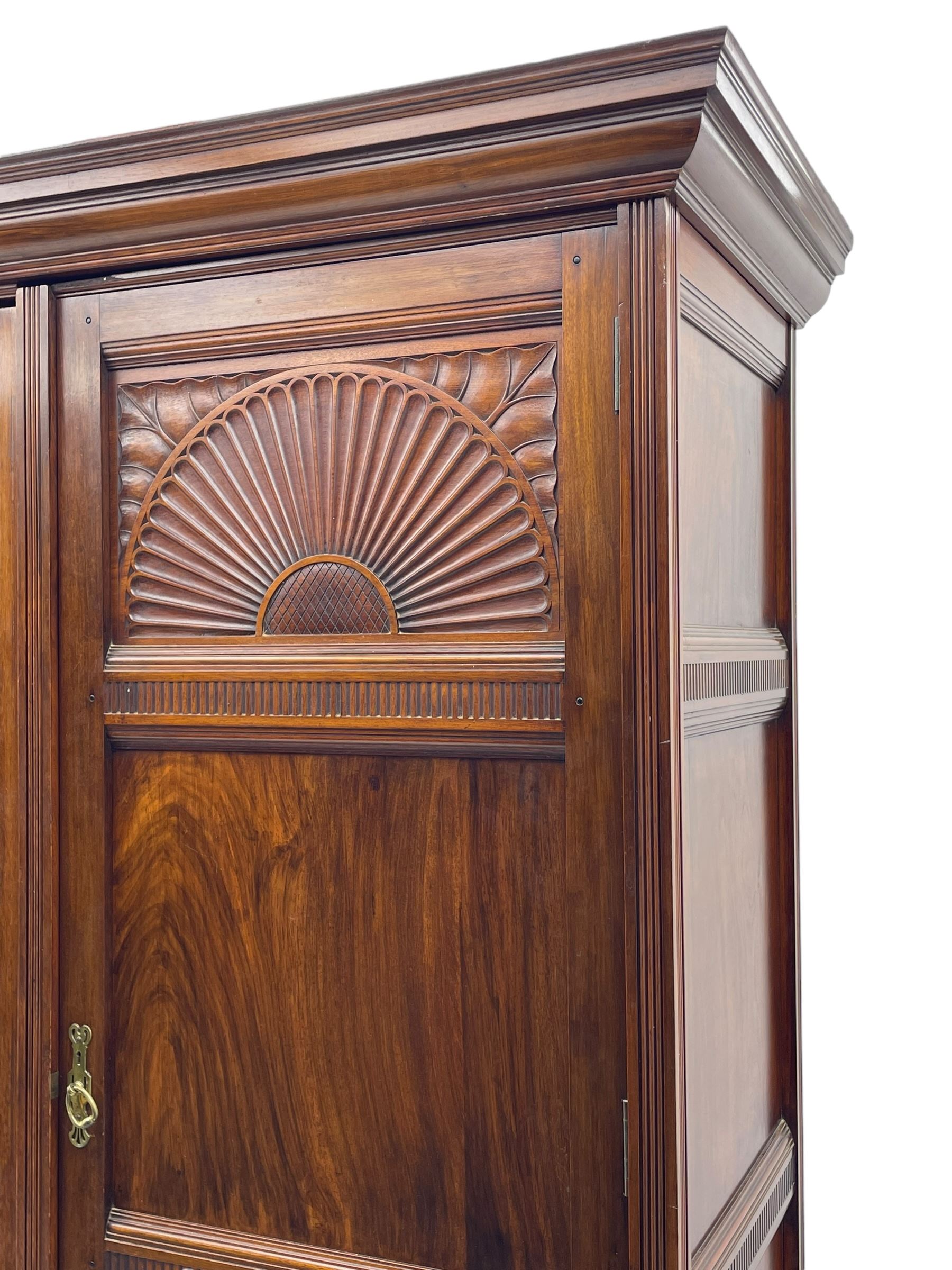 Late Victorian walnut triple wardrobe, projecting moulded cornice over central bevelled mirror door and flanking panelled doors, the top panels carved with fluted fans and stylised leaf motifs, the interior fitted with three linen slides, two drawers and hanging space, two long drawers to base, reed moulded uprights and vertical fluted horizontal rails 