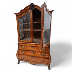 18th century Dutch marquetry walnut and gilt metal mounted vitrine cabinet on chest, shaped pediment carved with scrolling foliage cartouche, inlaid with trailing leafy branches and flower heads, two internal shelves enclosed by two glazed doors, the lower section with bombe outline fitted with three drawers, with ornate cast gilt metal edging and terminal caps