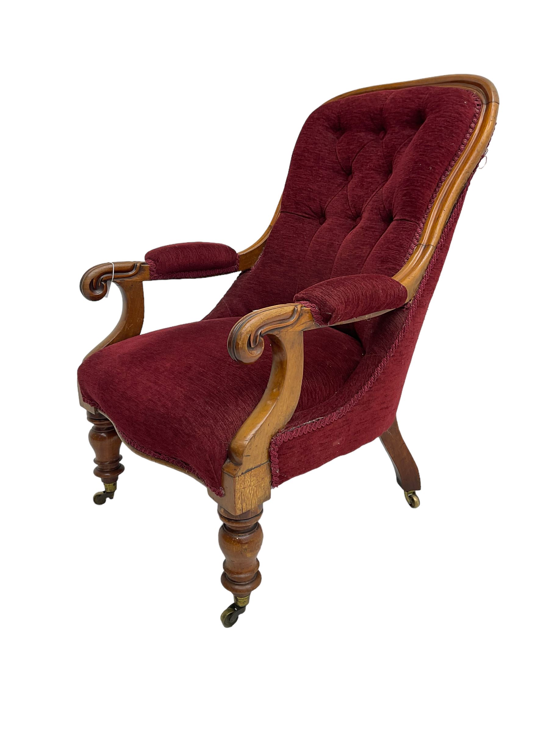 Victorian mahogany framed open armchair, upholstered in buttoned red fabric, the arm terminals carved with scrolls, on turned front supports with brass cups and castors