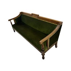 Late Victorian walnut framed sofa, rectangular backrest with carved detailing and central motif, upholstered in olive green fabric with brass studded trim and patterned front rail, scrolled fluted arms supported by turned uprights terminating in bun feet