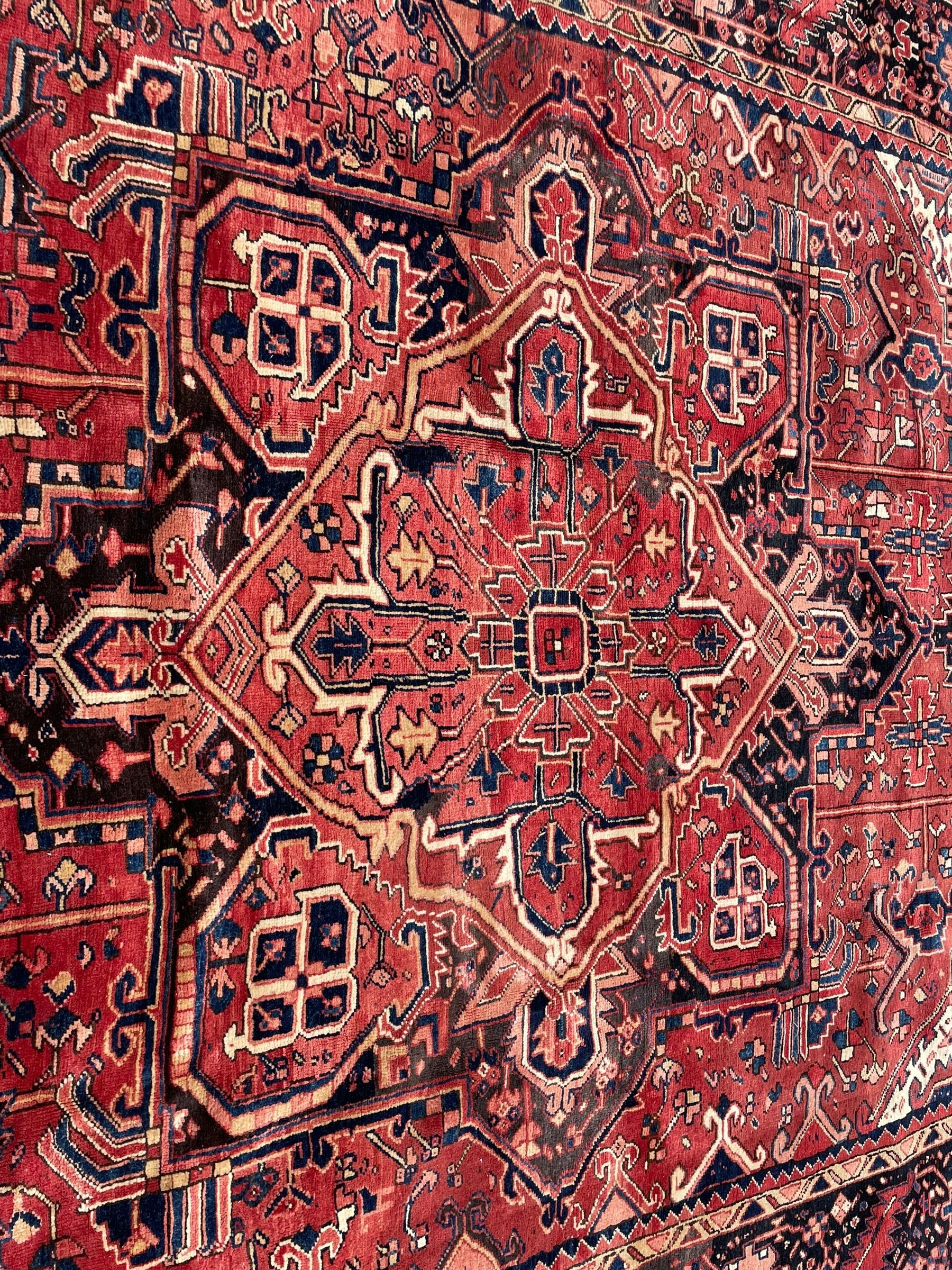 Persian Heriz red ground carpet, large central eight point medallion with projecting palmettes surrounded by small geometric motifs, decorated profusely with hooks, rosettes and animals, the busy border decorated with stylised foliate motifs within guard stripes 