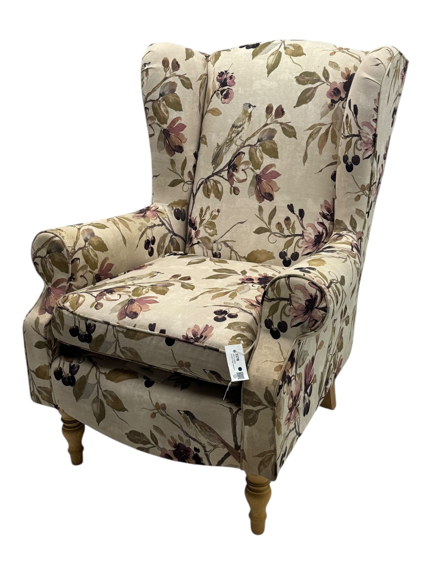 Hardwood-framed wingback armchair, upholstered in cream floral pattern fabric, on turned front feet