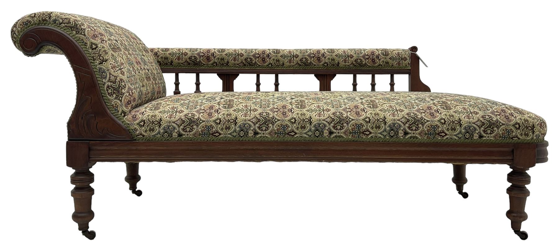 Late 19th century walnut framed chaise longue, upholstered in floral pattern fabric, rolled back rest and turned balustrade back, on turned feet with brass and ceramic castors 