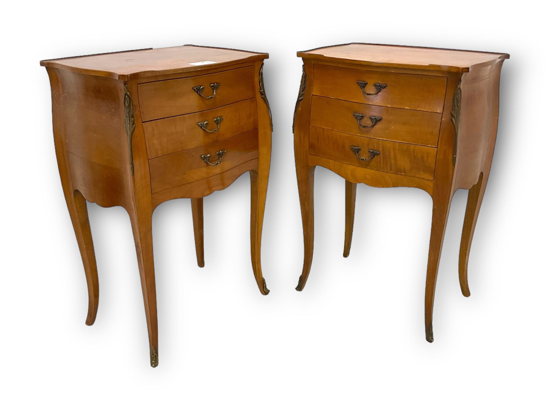 Pair of late 20th century French design cherry wood bedside lamp tables, shaped bombe form, fitted with three drawers, on tapering cabriole supports, decorated with ornate cast gilt metal mounts 