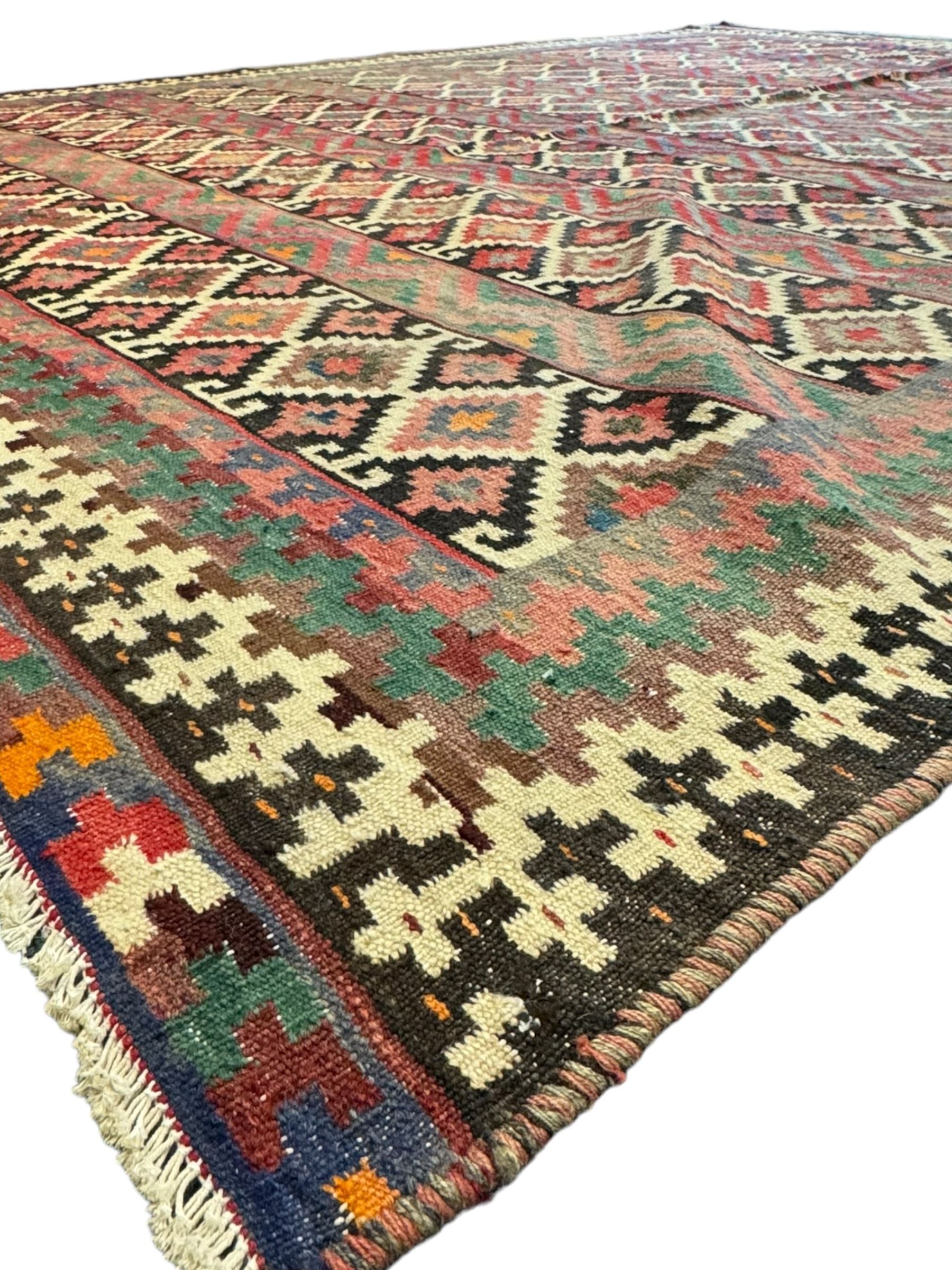 Northeast Persian Sumak Kilim red ground rug, the field decorated with rows of multicoloured diamond motifs featuring  geometric patterns, the border composed of alternating black and white stepped designs, enclosed by a narrow band with multicoloured geometric shapes