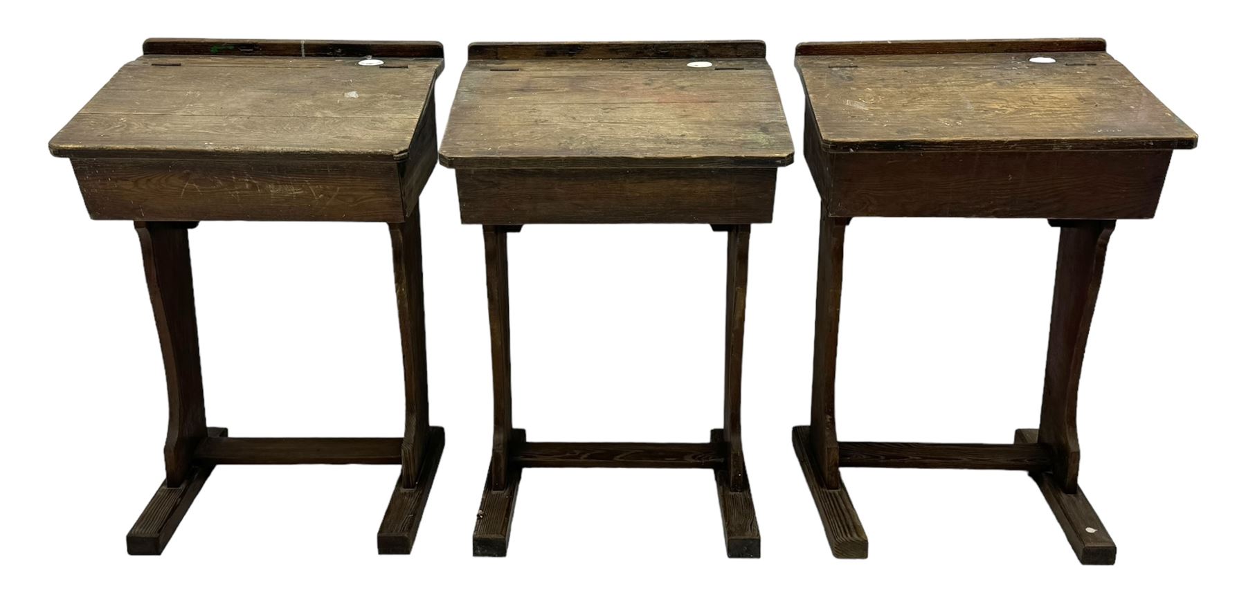 Three pitch pine school desks, each with rectangular lift-top with recessed ink well enclosing storage compartment, on trestle supports joined by stretcher