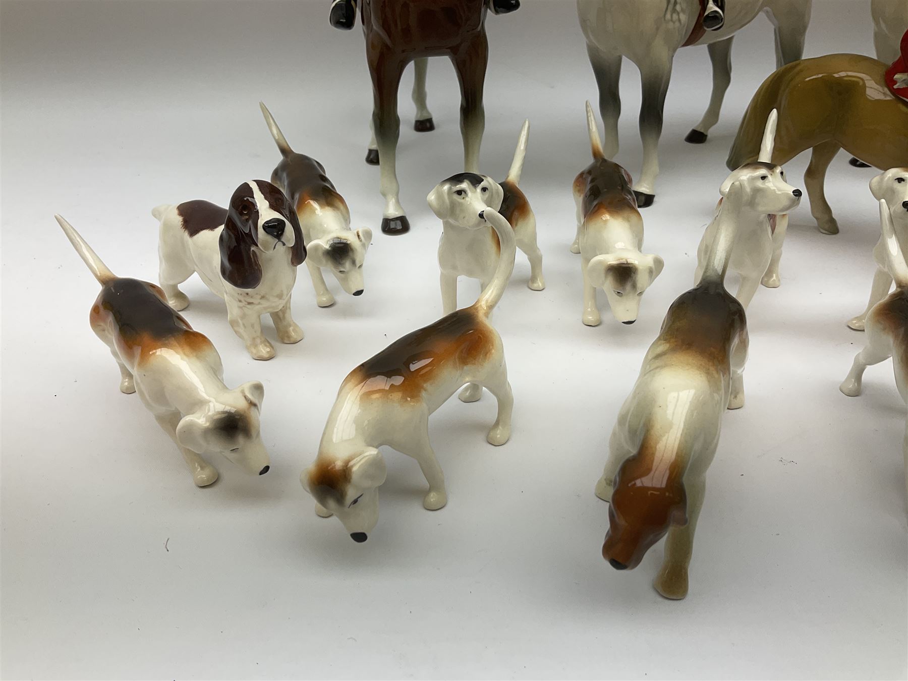 Beswick Hunting Group, comprising: two huntswoman on grey horses, model no 1730, huntsman on a bay horse, model no 1501, a seated fox, model no 1748, eighteen fox hounds and a spaniel, model no 967, all with printed marks beneath, together with three other ceramic huntsman on horseback and two hounds. 