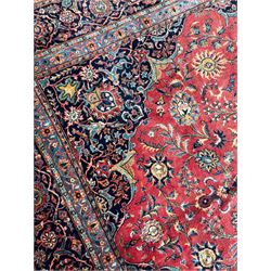 Persian Kashan crimson ground carpet, central rosette medallion on a field of trailing foliate branches decorated with palmettes, scrolling border with repeating plant motifs and flower heads, enclosed within floral pattern guard stripes