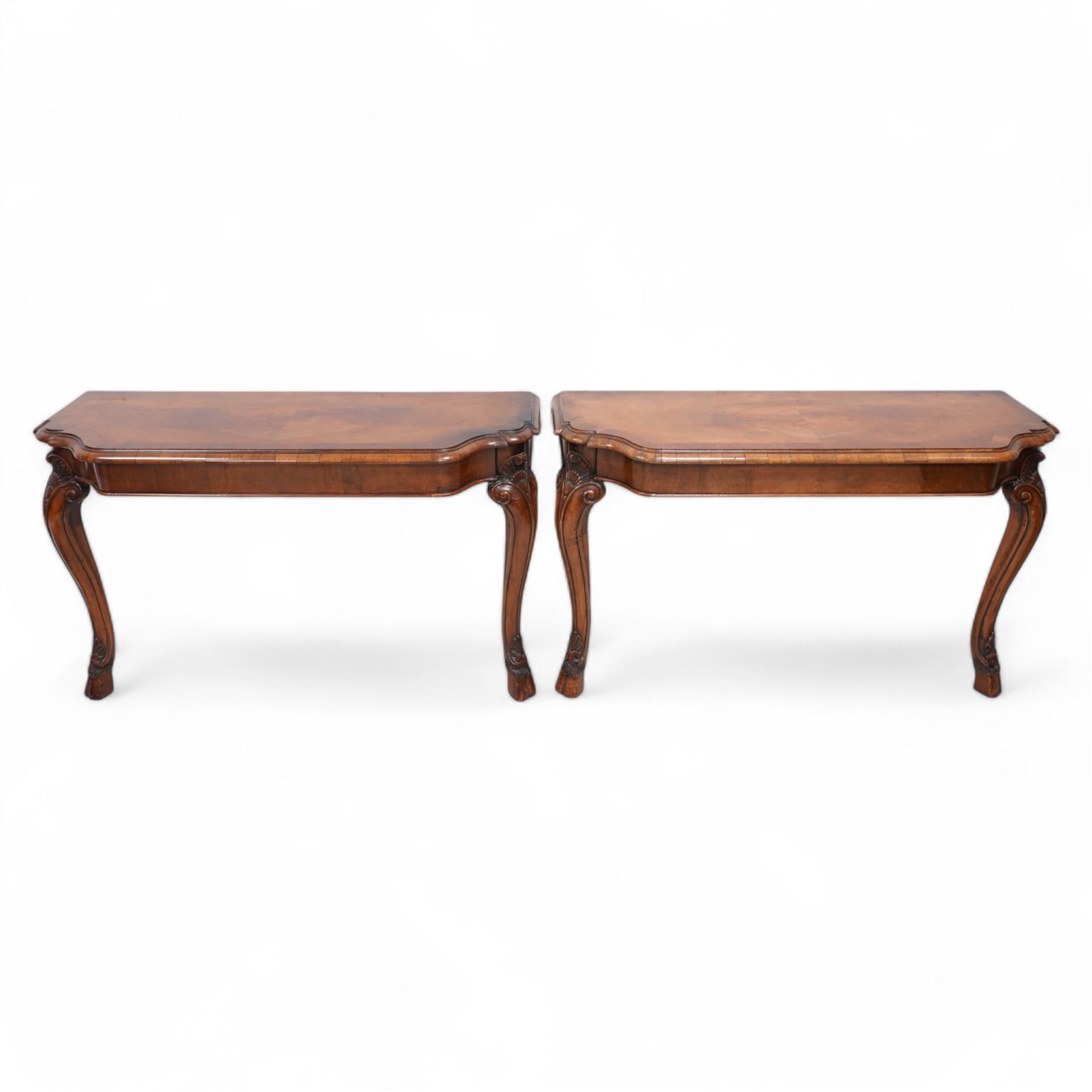 Pair of Georgian walnut console tables, the shaped rectangular cross-banded top with moulded edge over a banded frieze, raised on moulded cabriole supports decorated with scalloped shell and scroll carved knees, terminating to hairy hoof feet