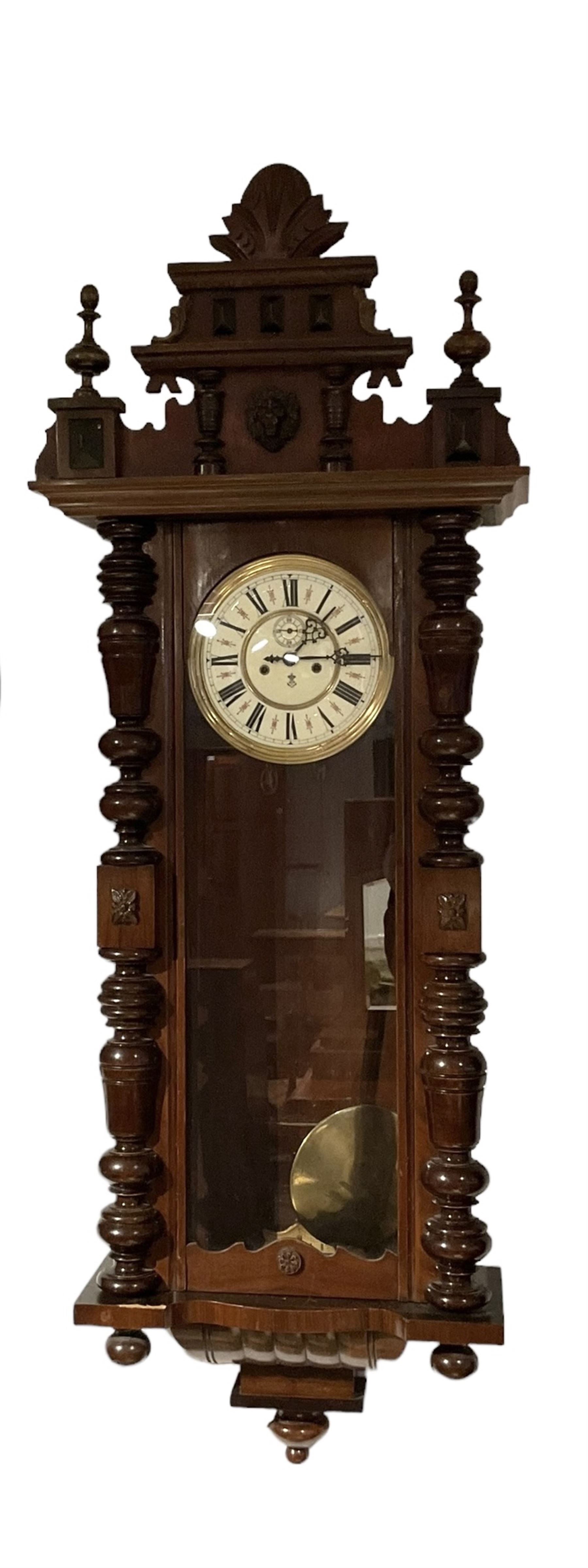 Gustav Becker -  German weight-driven 8-day wall clock in a walnut and ebonised case with a carved pediment and finials, fully glazed case door with visible pendulum and two brass cased weights, two  part dial with seconds hand, Roman numerals and pierced steel hands, rack striking movement with a deadbeat escapement.