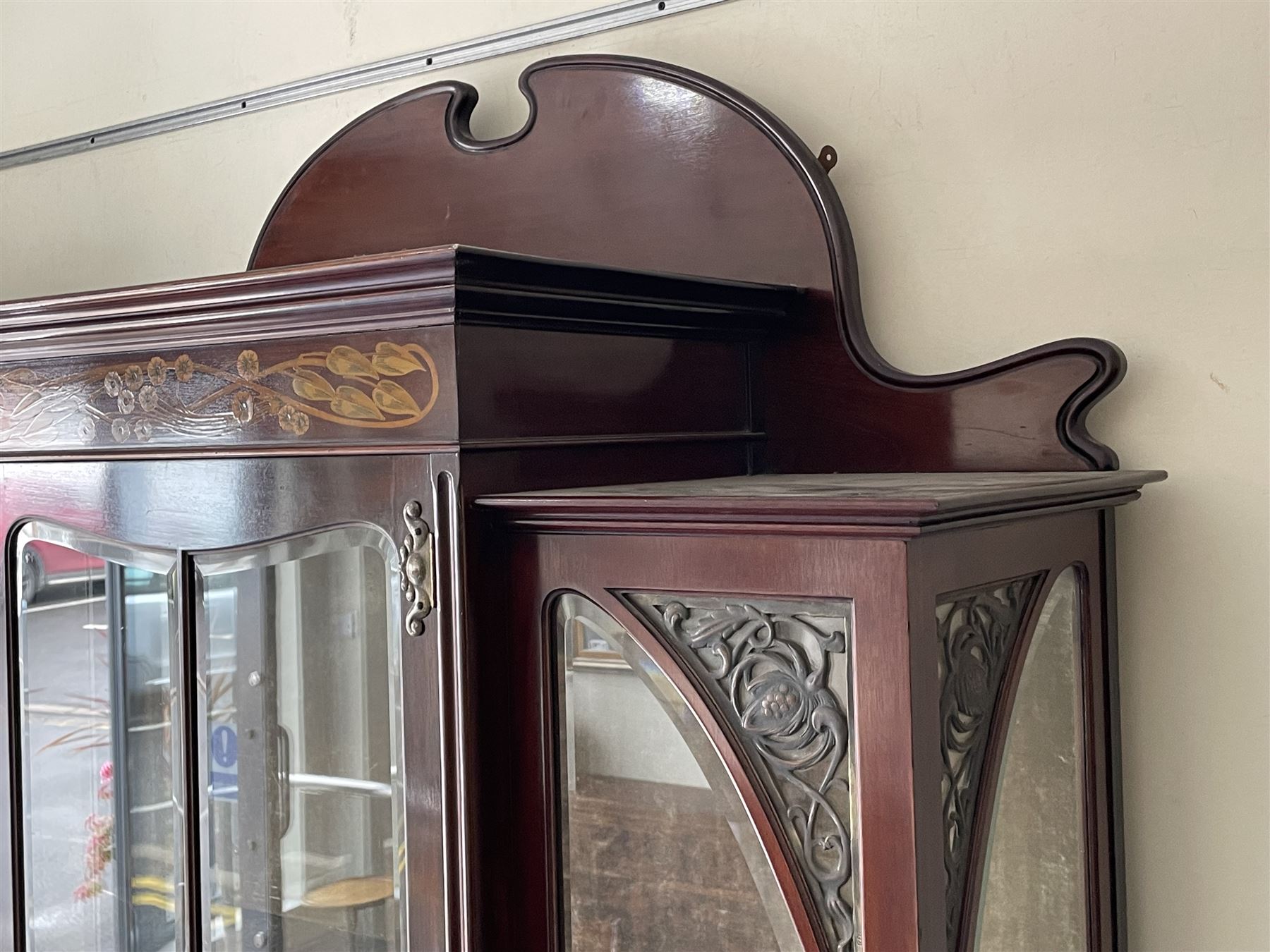 Art Nouveau period inlaid mahogany display cabinet, raised shaped and moulded pediment over projecting moulded cornices, the upper frieze inlaid with trailing branches and tulips, single astragal and bevel glazed door enclosed velvet lined interior fitted with shelves, flanked by curved glass panes decorated with pierced metal foliate spandrels, lower flanking shelves with mirror backs enclosed within shaped and pierced rails inlaid with flower heads, on tapering octagonal supports terminating to compressed pad feet, the lock stamped 'Salmon Bros, London' 