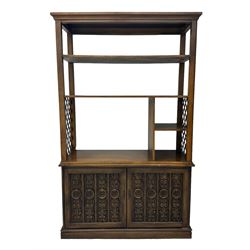 Mid 20th century oak bookcase cupboard, projecting cornice over three open shelves with subdivided sections and latticework uprights, two doors to the base with floral and scrollwork carvings and central brass handles, resting on a moulded plinth base