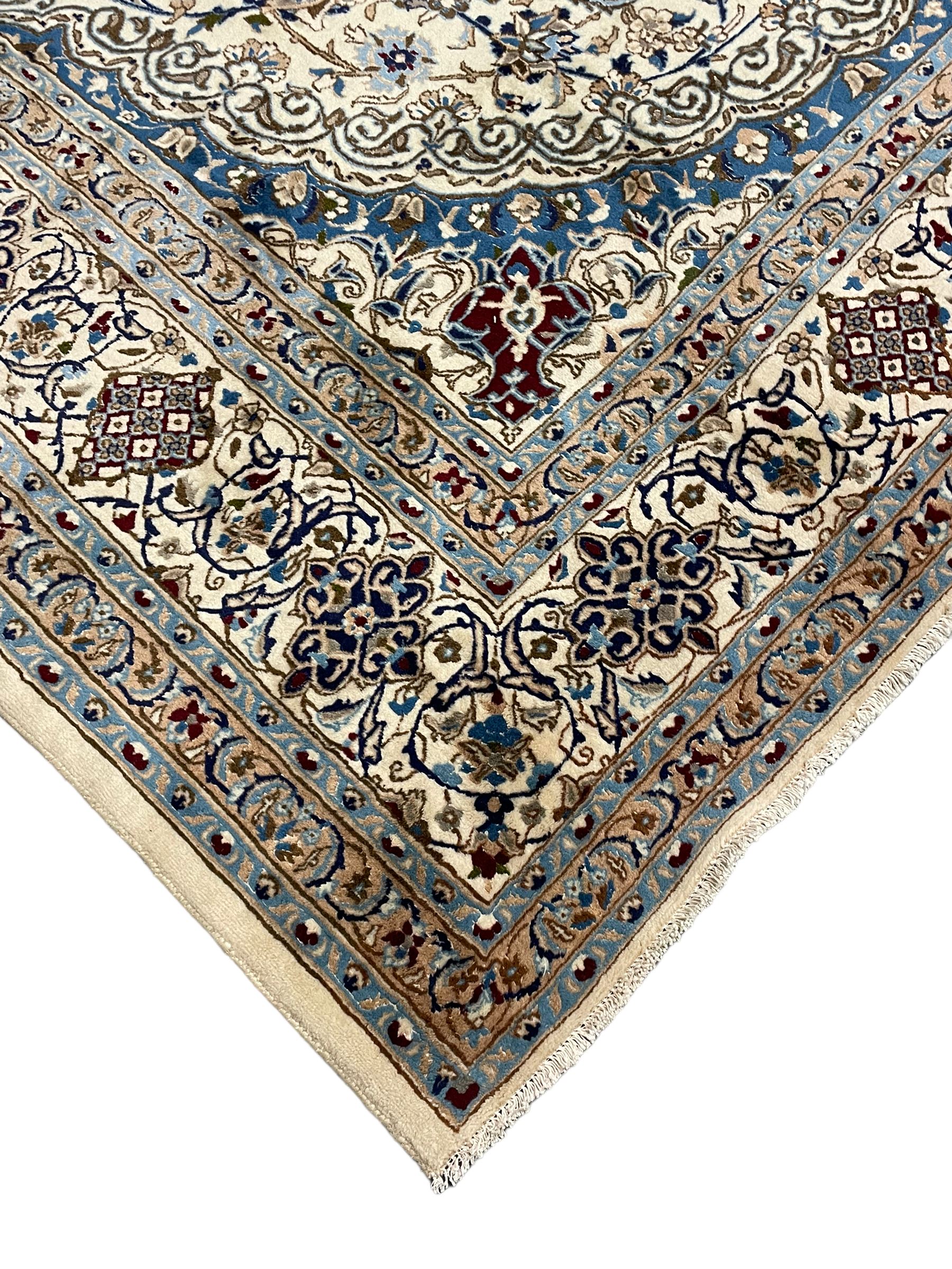 Persian Nain ivory ground carpet, the field decorated all over with leafy branches and stylised flower head motifs, blue ground central medallion and matching spandrels decorated with trailing foliate pattern, repeating guarded border with overall floral design