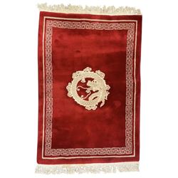 Chinese washed woolen red ground rug, central circular dragon motif in ivory, framed by a decorative Greek key border in matching ivory tones, finished with fringed ends