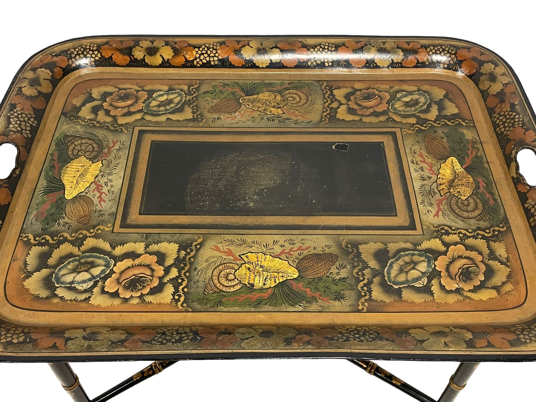 19th century tole ware tray of rectangular form, decorated with Japanese inspired floral motifs and gilt shells, with pierced handles, the associated ebonised and gilt stand, raised on ring turned splayed supports united by X-stretcher, decorated with gilt foliage