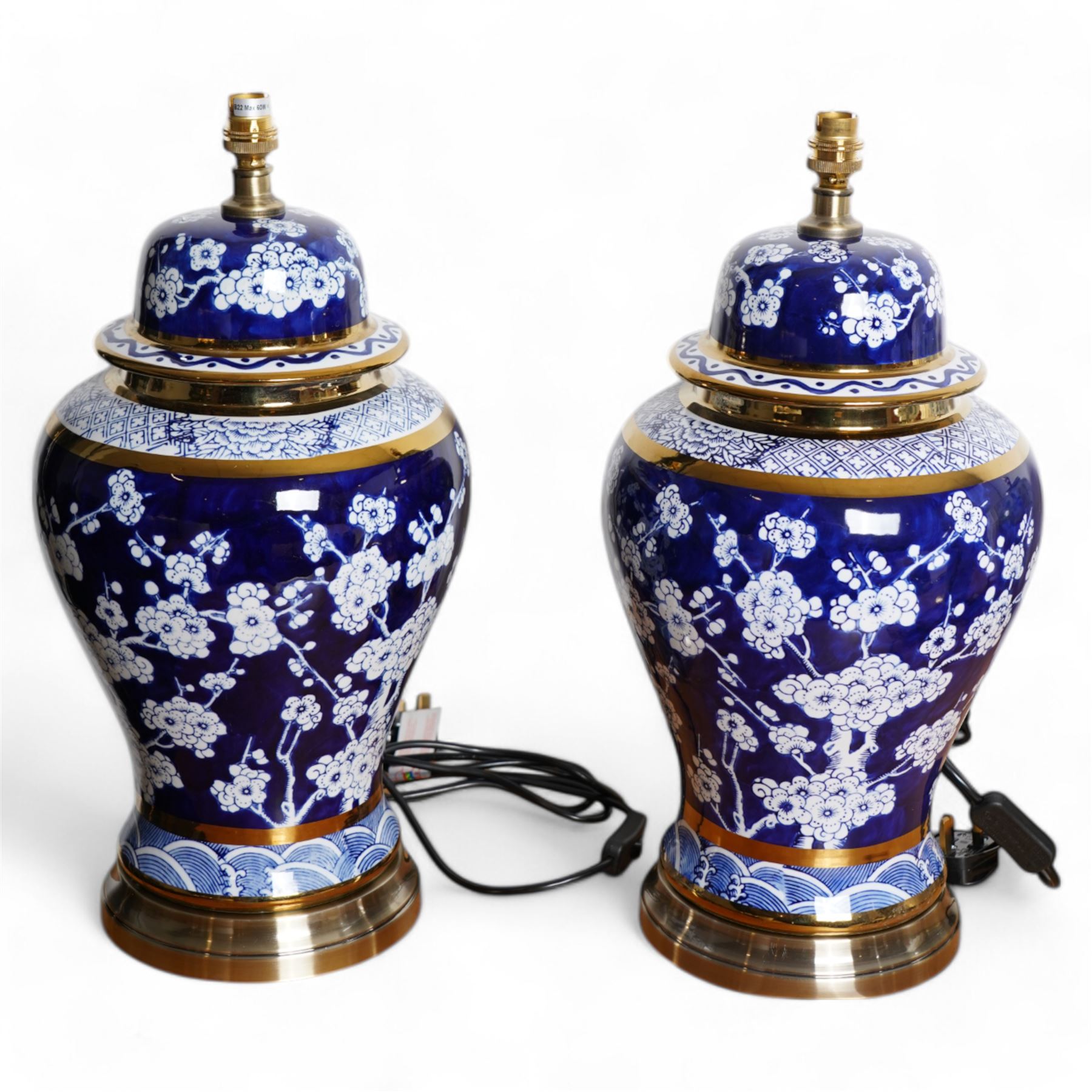 Pair of blue and white table lamps, each in the form of a vase and cover, decorated with cherry blossom, within foliate and geometric borders, raised upon circular gilt bases, H48cm including shades