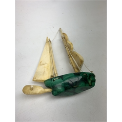 A Japanese carved ivory model of a sailing boat, surmounted by three carved figures (a/f), L22.5cm, together with a smaller sail boat with malachite hull and ivory sails and rudder, H18cm. 