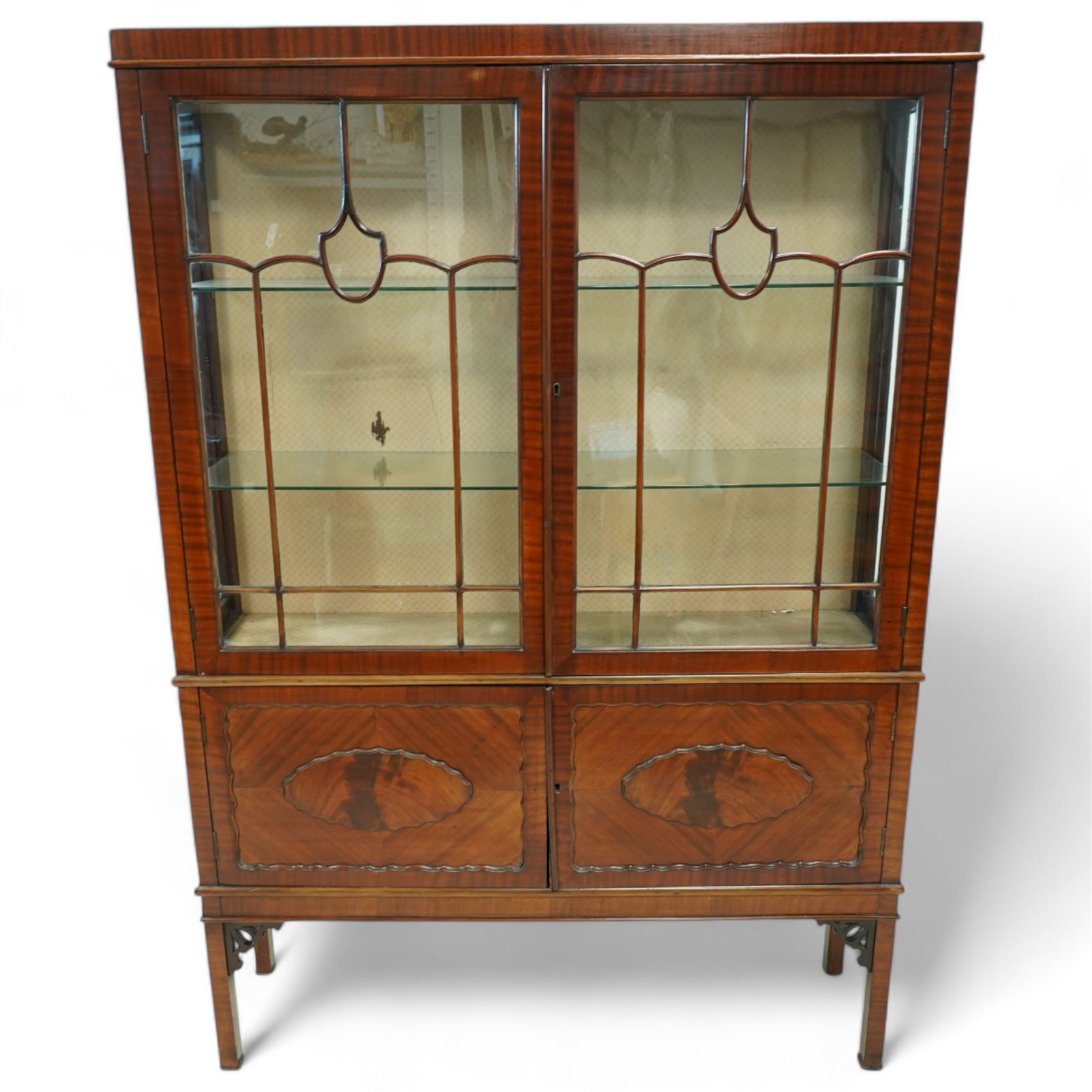 Early 20th century mahogany display cabinet, enclosed by astragal glazed doors over two scalloped panelled cupboard doors, on square supports with pierced scrolling brackets