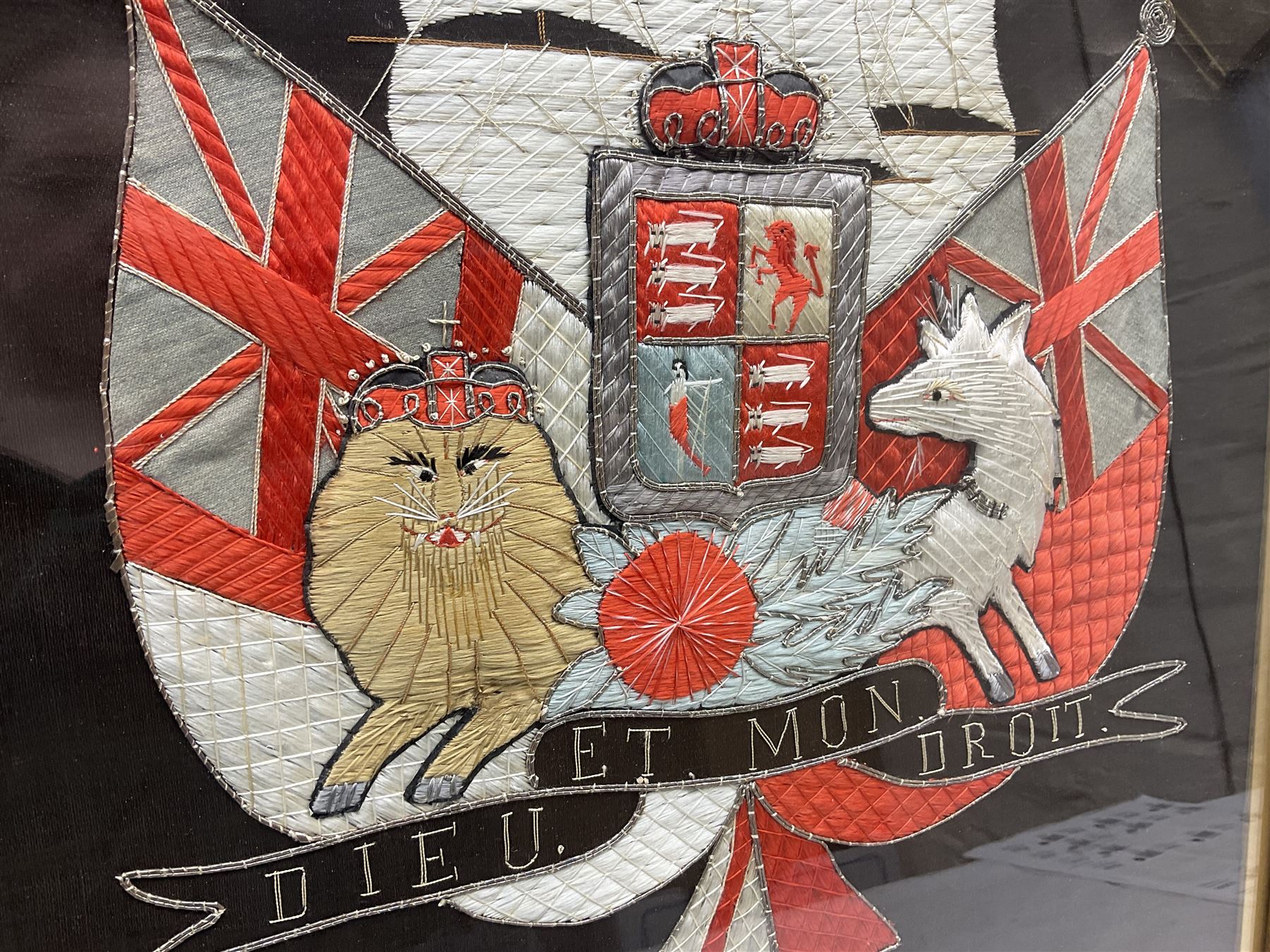 Early 20th century silk needlework panel, depicting a ship in full sail and Royal Coat of Arms to centre, with red and white ensigns to either side, lion and unicorn below with quote 'Dieu Et Mon Droit', upon a black silk ground within gilt frame, H59cm