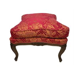 Late 20th century French design stained beech framed armchair and matching stool - the armchair with shaped and moulded frame carved with flower heads and foliage, upholstered in silk red and gold ground fabric with floral pattern, on scroll carved cabriole feet decorated with flower head carvings (W73cm, H82cm, D75cm); the footstool of concaved rectangular form with moulded frame carved with flower heads, upholstered loose cushion, on cabriole feet (70cm x 64cm, H48cm)