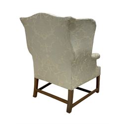 Georgian mahogany framed wingback armchair, upholstered in floral pattern silk damask fabric, wide seat enclosed by rolled arms, on chamfered square supports united by plain stretchers 