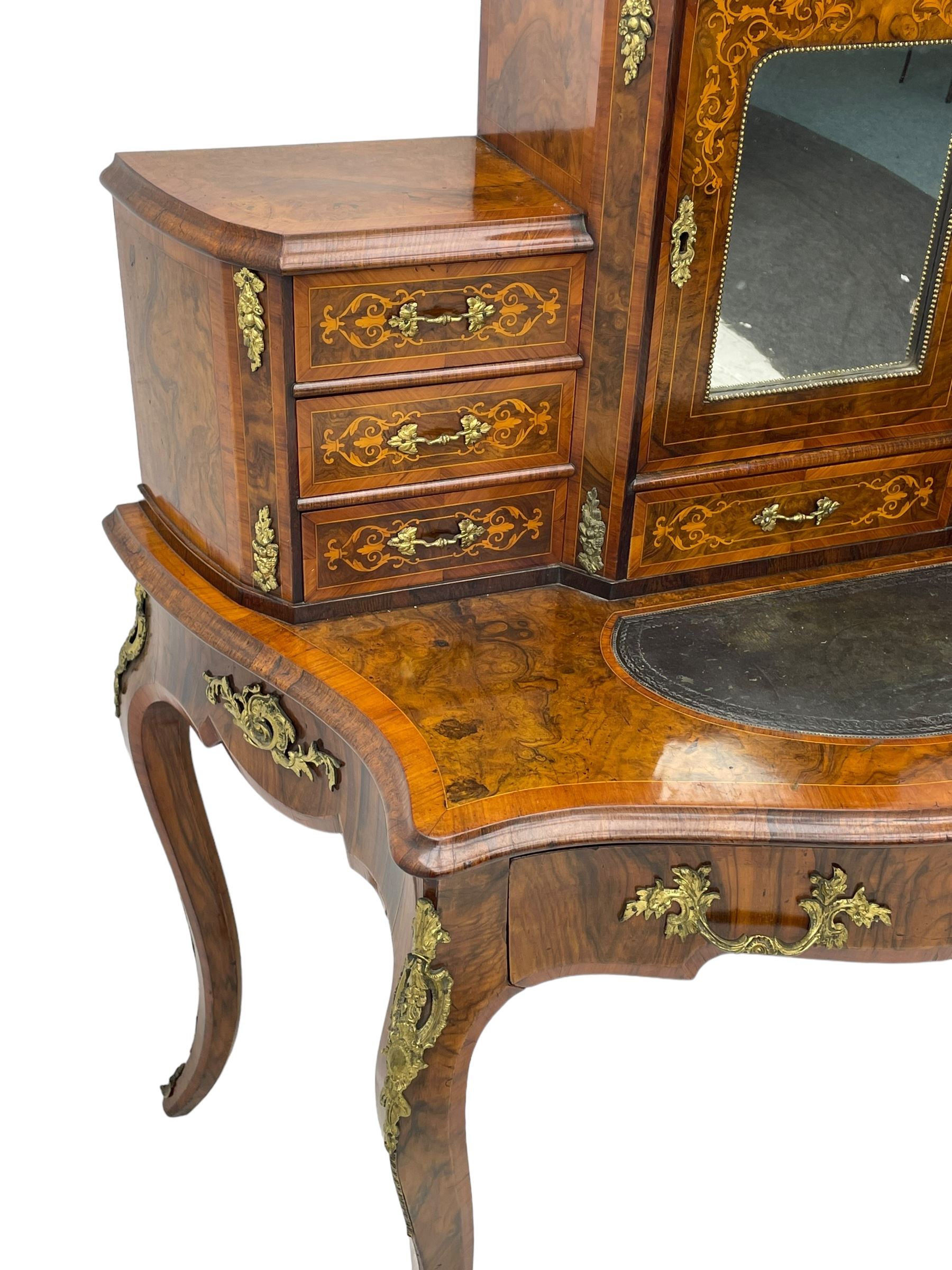 19th century French figured walnut Bonheur de Jour or writing desk, the upper section with brass gallery over mirror glazed cupboard and a combination of drawers, shaped and moulded top with leather inset and satinwood band, fitted with single drawer, on cabriole supports, inlaid throughout with scrolling foliate decoration in boxwood, ornate cast brass mounts 