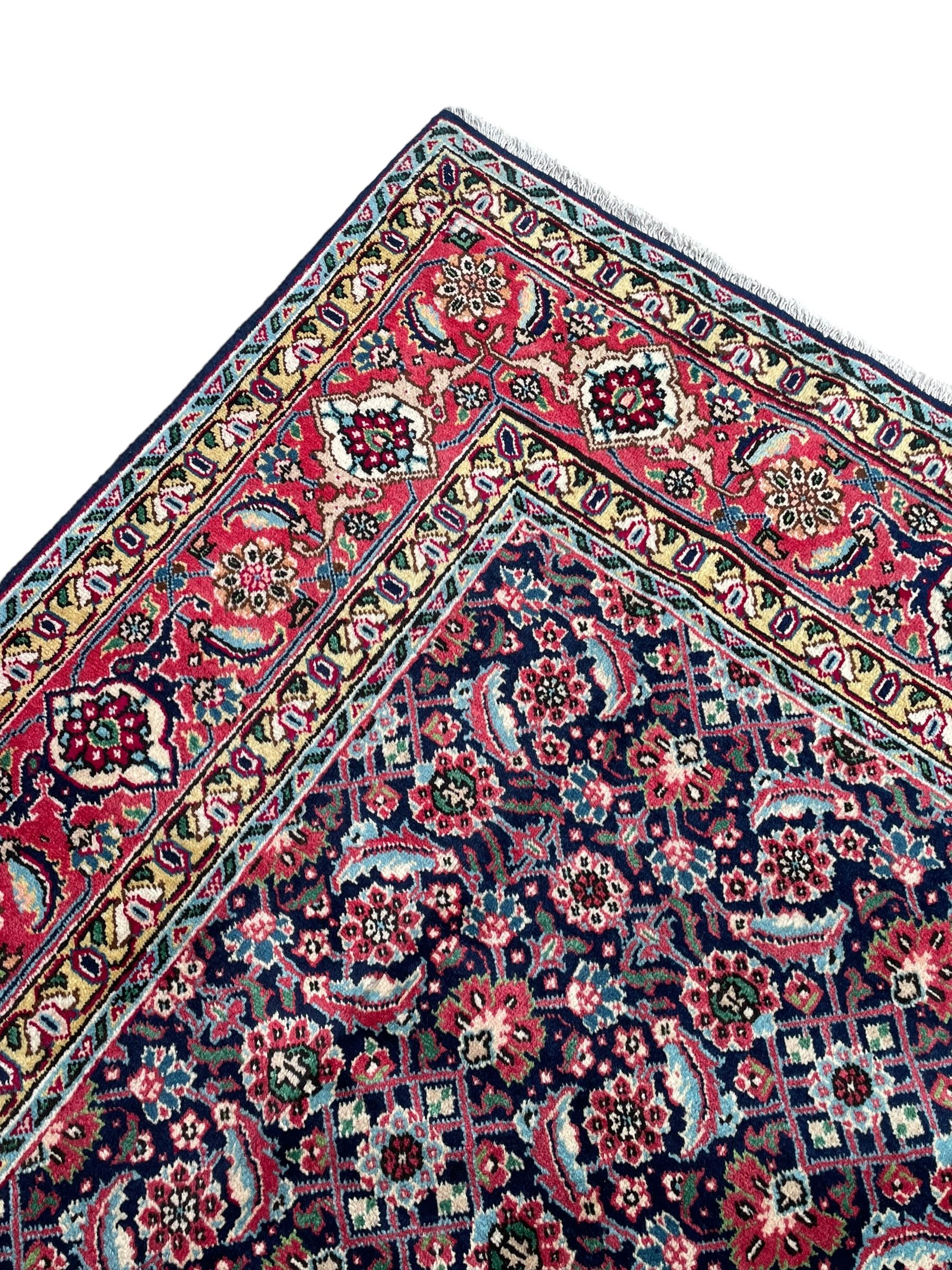 Persian Farahan indigo ground rug, the field decorated with large repeating floral herati motifs, crimson ground border decorated with palmettes and trailing leafy branch, within guard stripes 