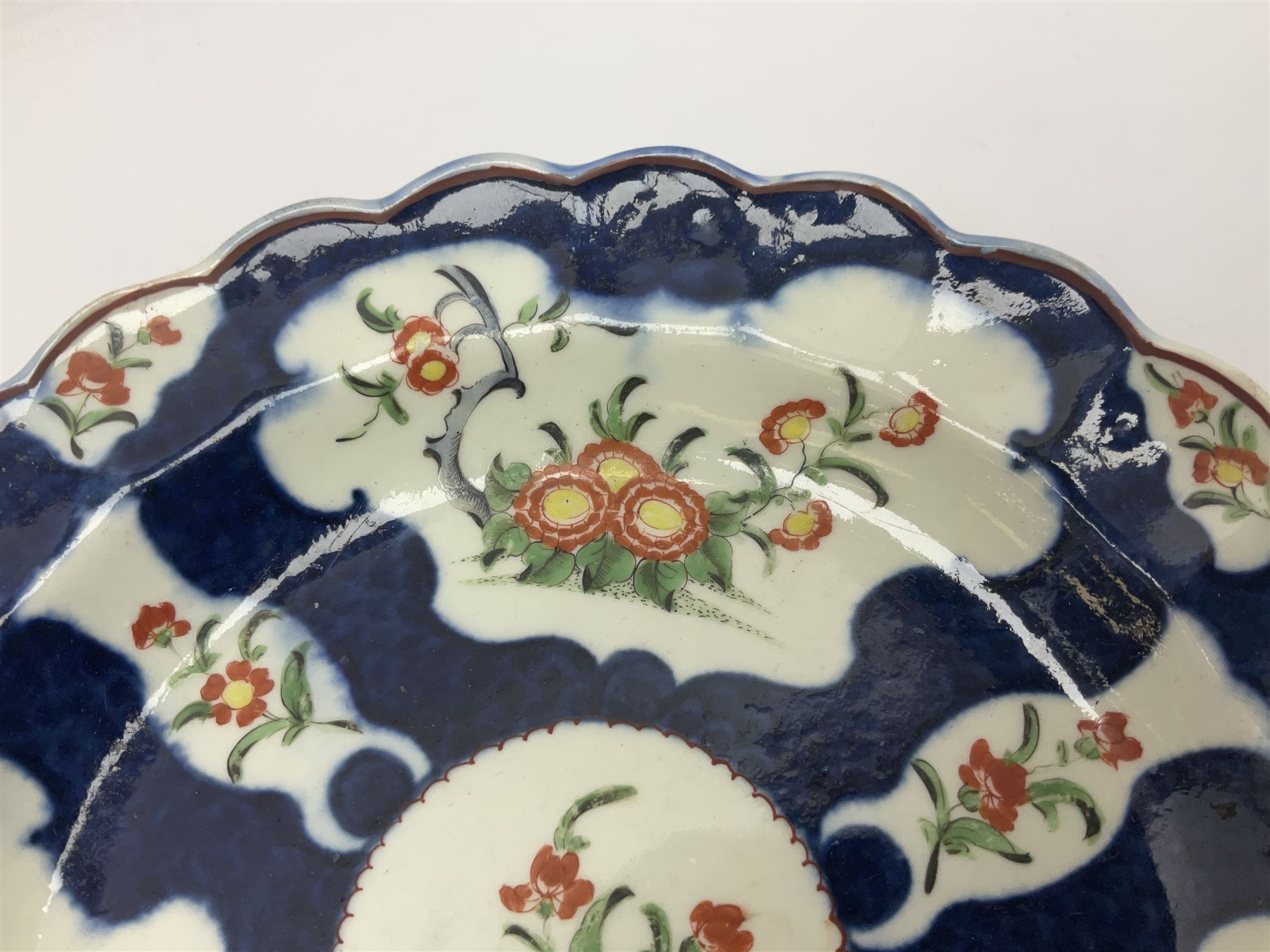 Three 18th century Worcester desert dishes, the first example decorated in the Scarlet Japan pattern, circa 1790, painted with alternating panels of Kakiemon style prunus blossom and chrysanthemum, and orange ground panels with gilt fret detail, D19cm, the second example, circa 1770, decorated with Kakiemon style chrysanthemums and foliage within shaped reserves upon a blue scale ground, with fretted square pseudo mark beneath, D19cm, and the third, circa 1770, painted with polychrome floral sprays and sprigs, D20cm