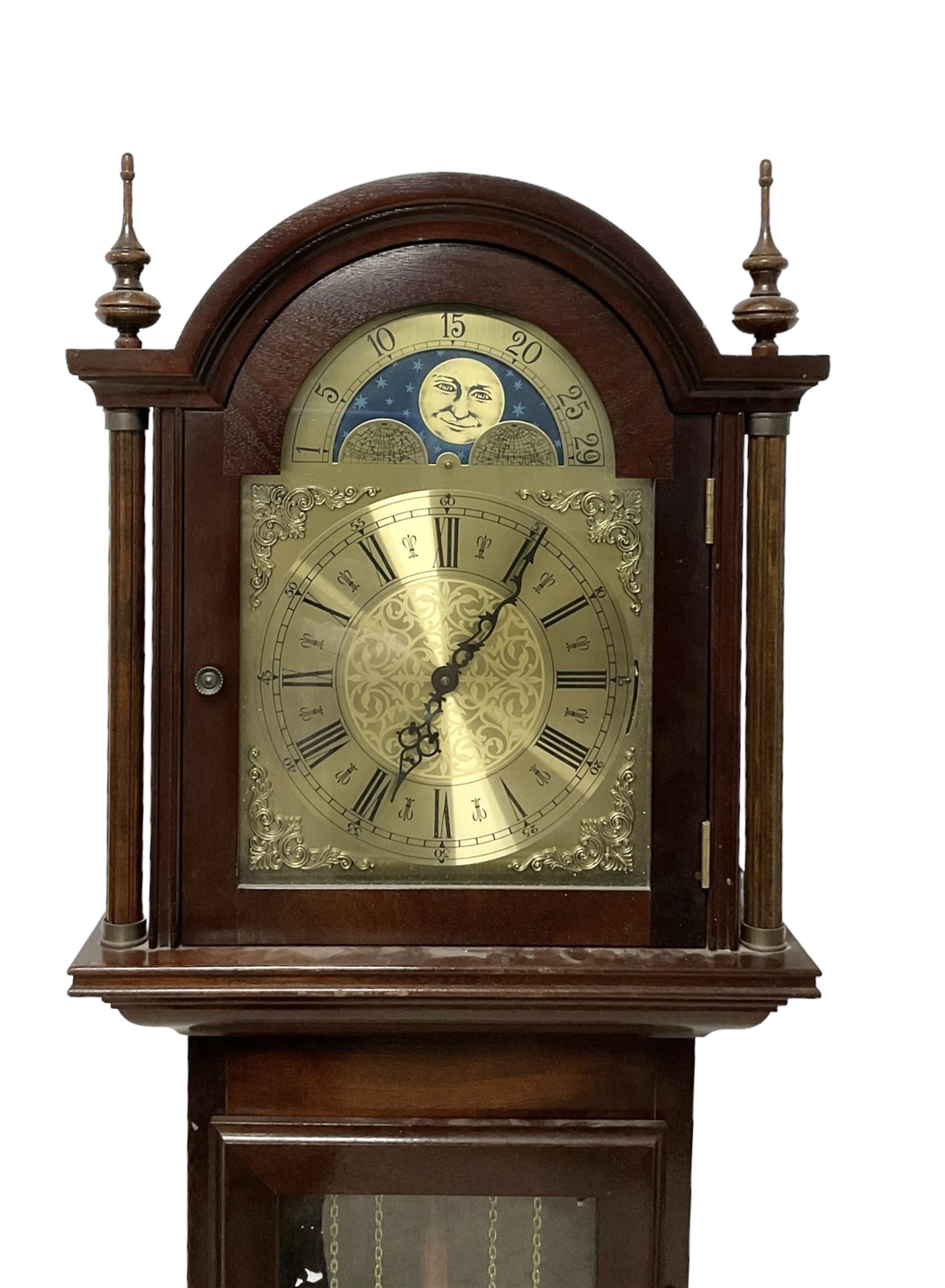 20th century - Westminster chime 8-day grandmother clock in a mahogany case, with a break arch top and brass finials, fully glazed trunk door with visible brass cased weights and pendulum, brass dial with etched dial centre and spandrels, chapter ring with Roman numerals and working moon disc to the arch, two train chain driven movement with 12 gong rods and chime selection for the quarters and hours.